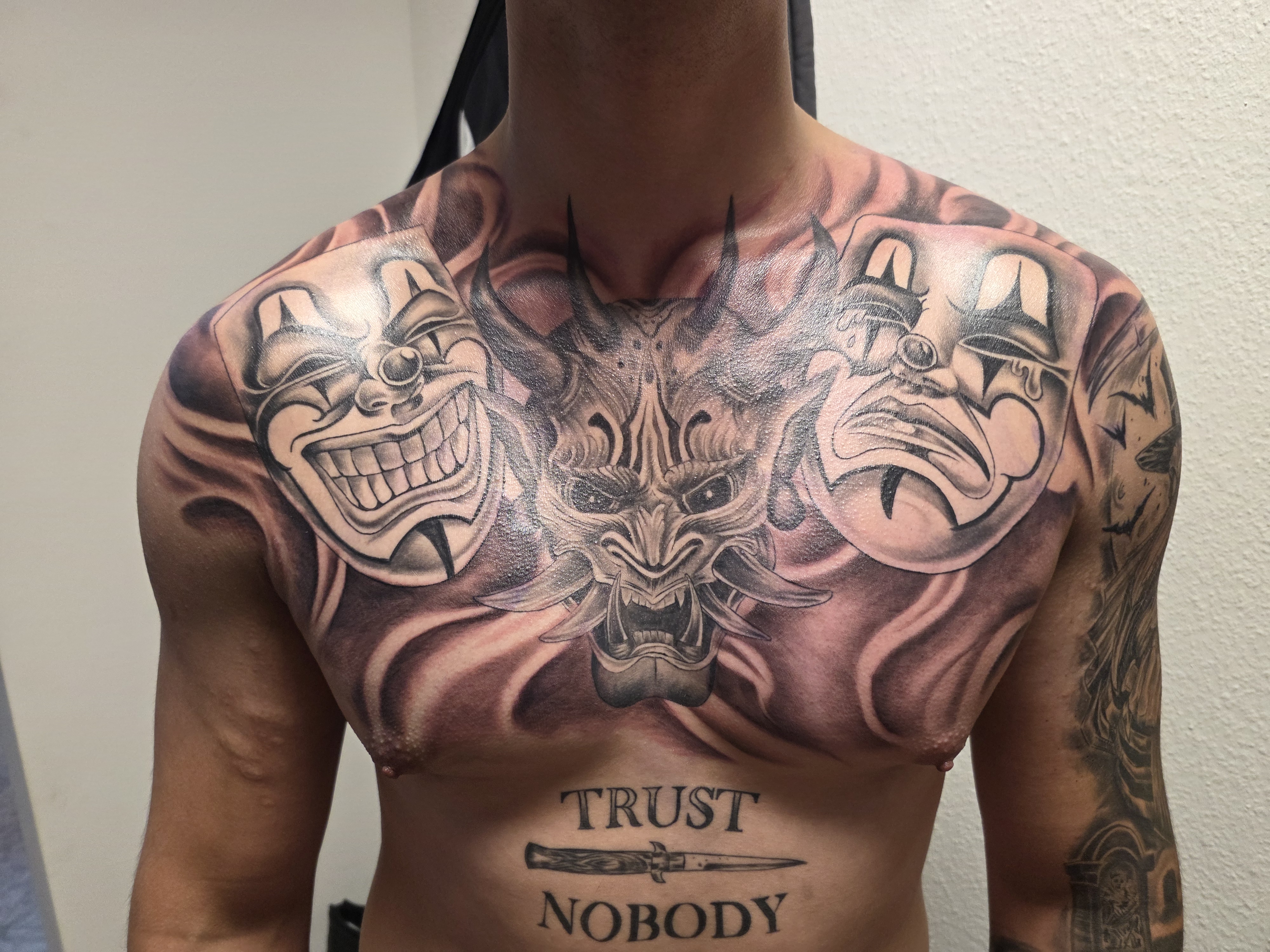 Black & Grey Tattoo – zwei Clownsmasken mit Teufelsgesicht in der Mitte, detailreiche Schattierungen – Saints Tattoo Pirna